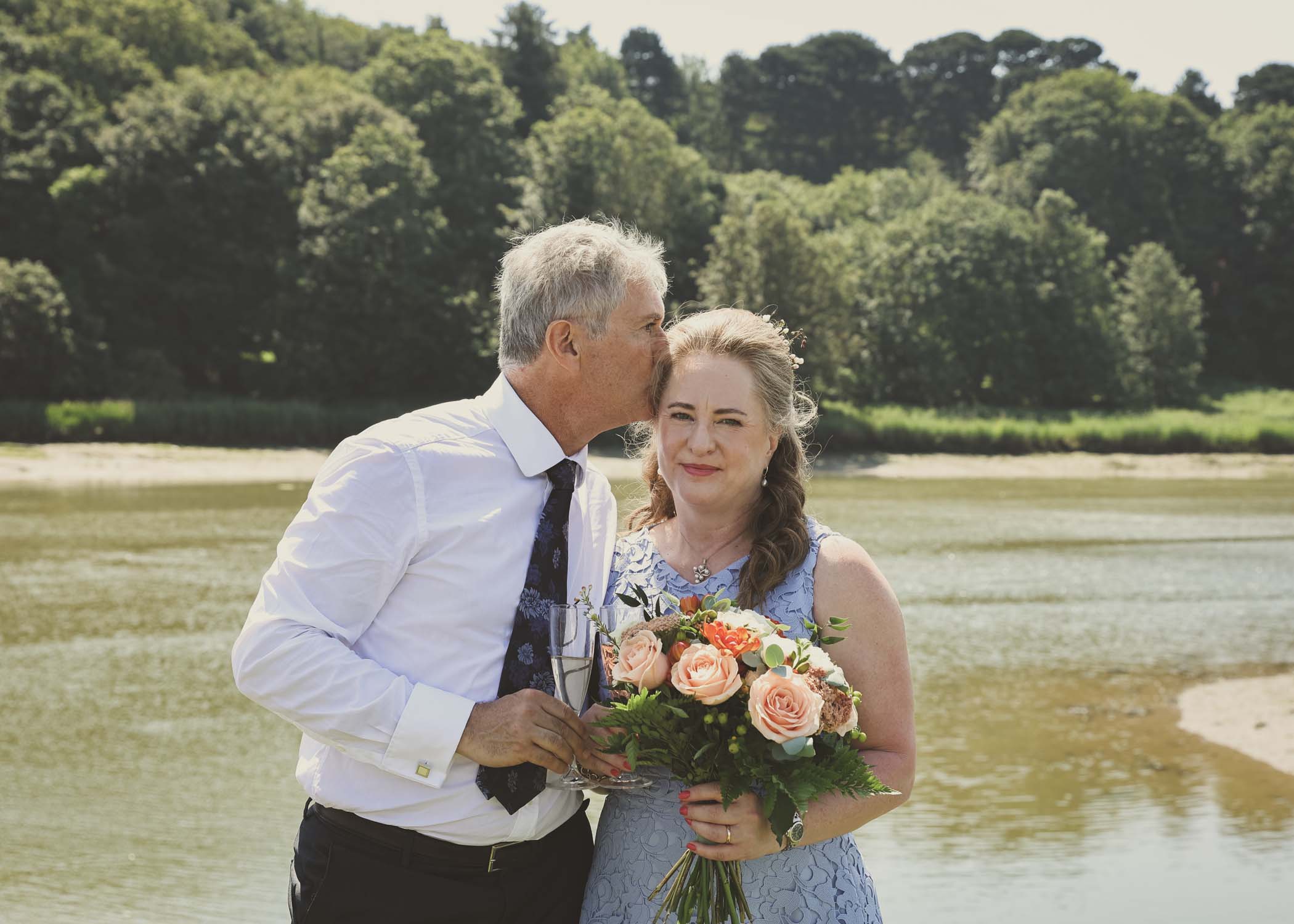 A groom kissing his bride on the head on the penisula at woodbridge marina on a wedding day in Woodbridge captured by Suffolk Wedding Photographer Hayley Denston Photography